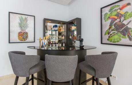 Home bar made out of dark wood with dark grey bar stools and artworks on the wall - Originals Interiors