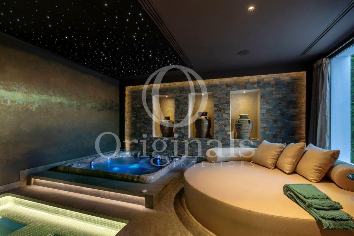 Swimming pool area with rough golden wall a round beige sofa, a hot tub and ancient decoration - Originals Interiors