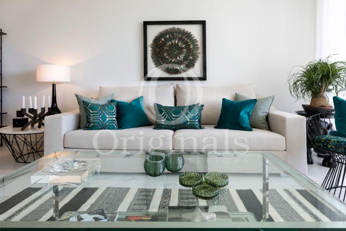 Living area with a beige couch, a glass coffee table, turquoise cushions and an artwork on the wall - Originals Interiors