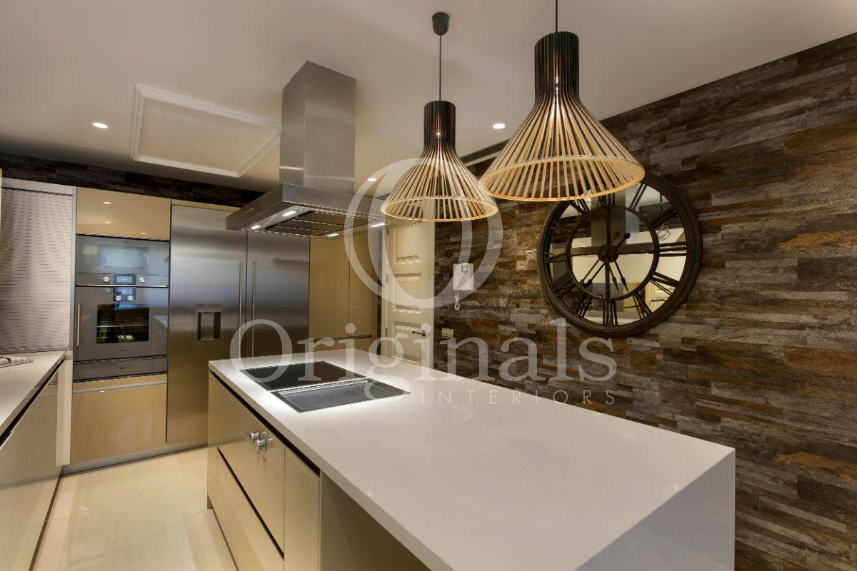 Kitchen with glittering white elements and a wooden patterned background with a mirroring clock on the wall - Originals Interiors